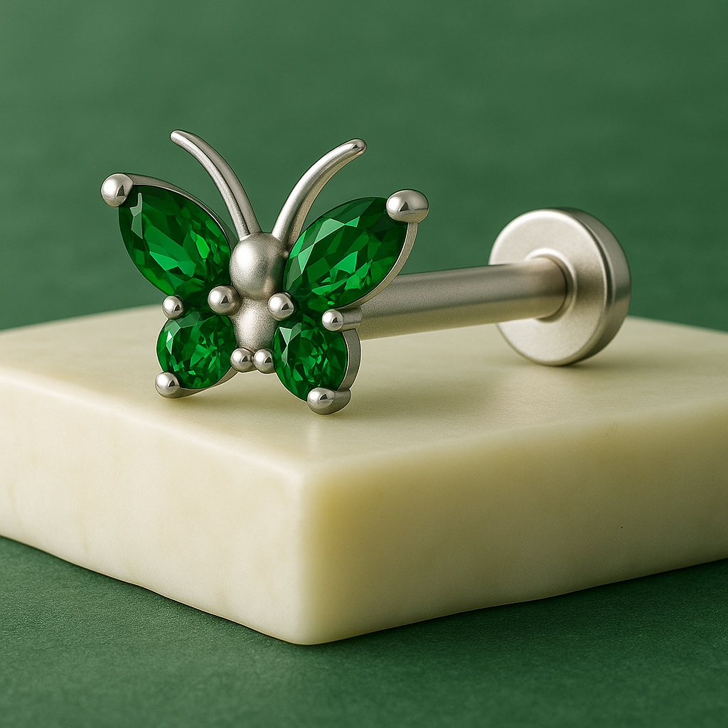 Butterfly-shaped earring with green gemstones on a beige block against a green background