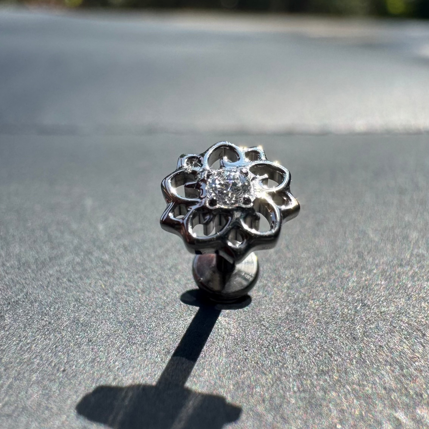 Silver flower-shaped earring on a reflective surface with blurred greenery in the background