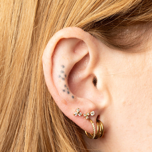 Close-up of an ear with gold vera hoop earrings and a trinity earrings.