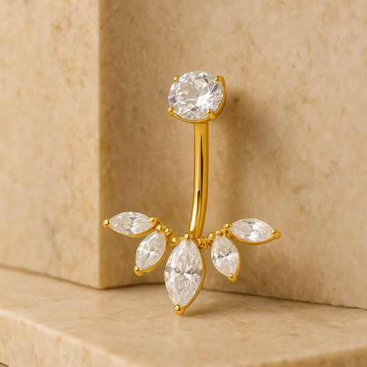 Gold belly button ring with clear gemstones on a beige stone surface