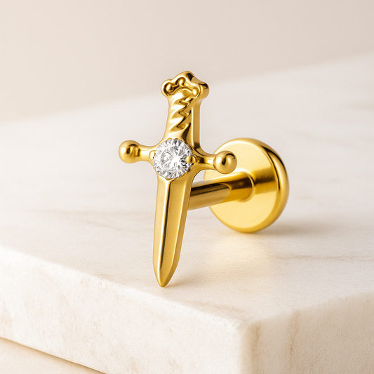 Gold sword stud earring with a diamond on a light beige background