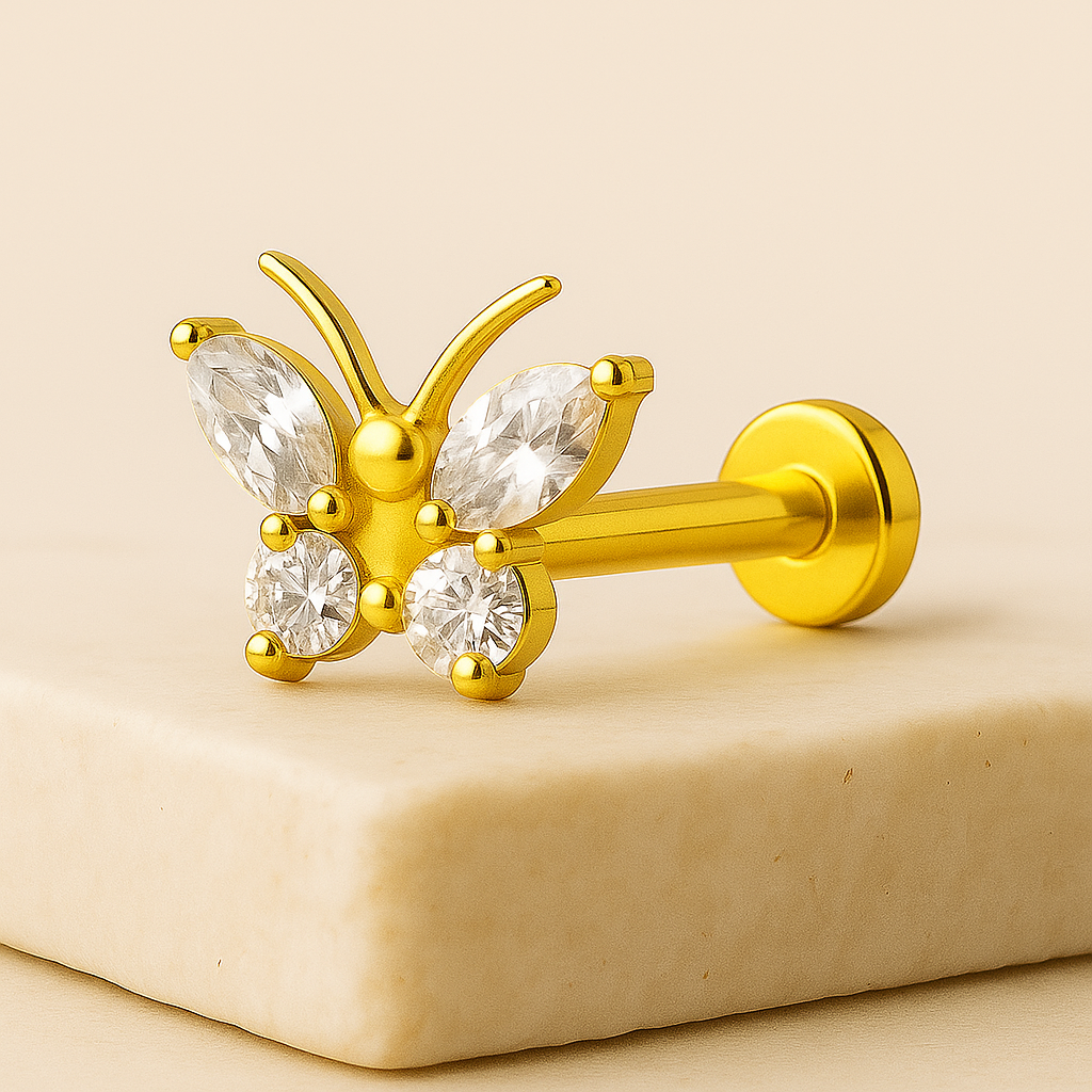Gold butterfly-shaped earring with clear gemstones on a beige stone surface