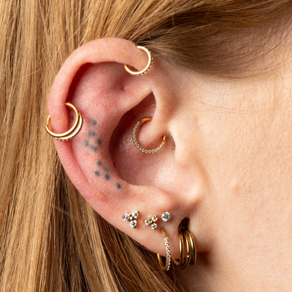 Close-up of an ear with multiple gold earrings with Daith and Helix piercing