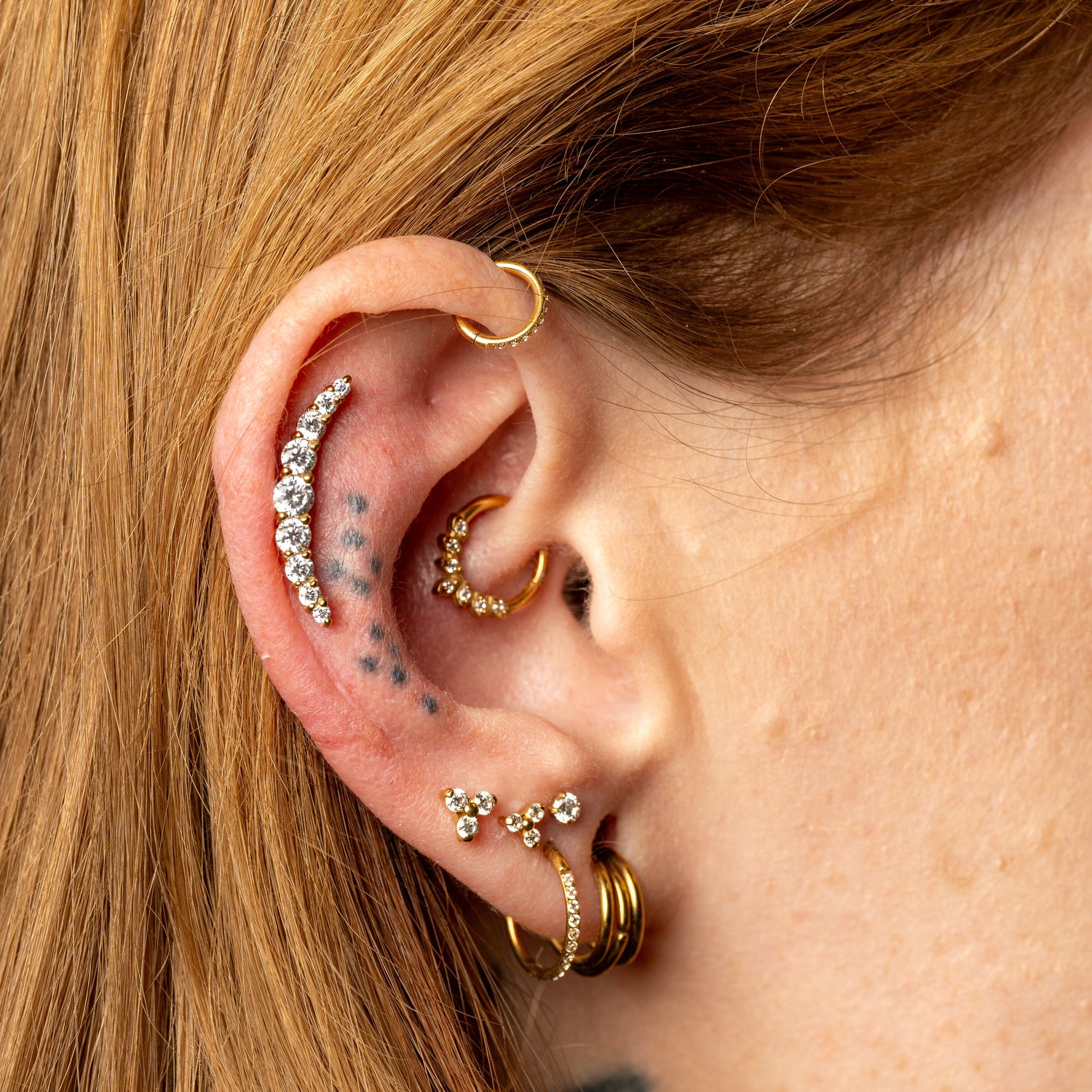 Close-up of an ear with multiple gold and silver earrings against a blurred background