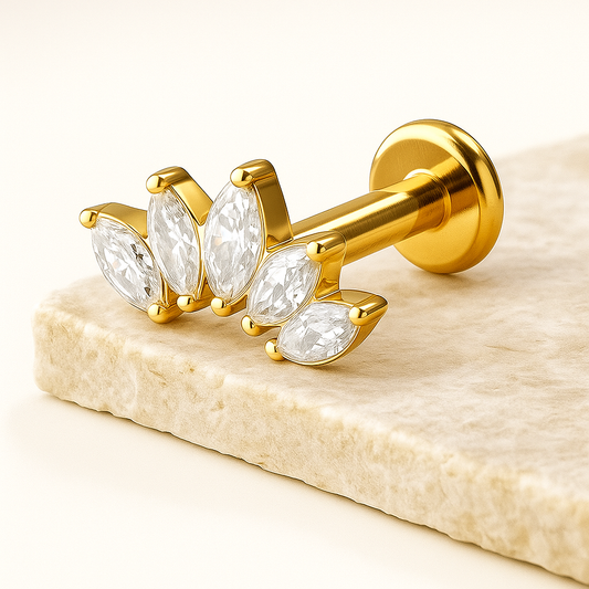 Gold earring with clear gemstones on a beige stone surface