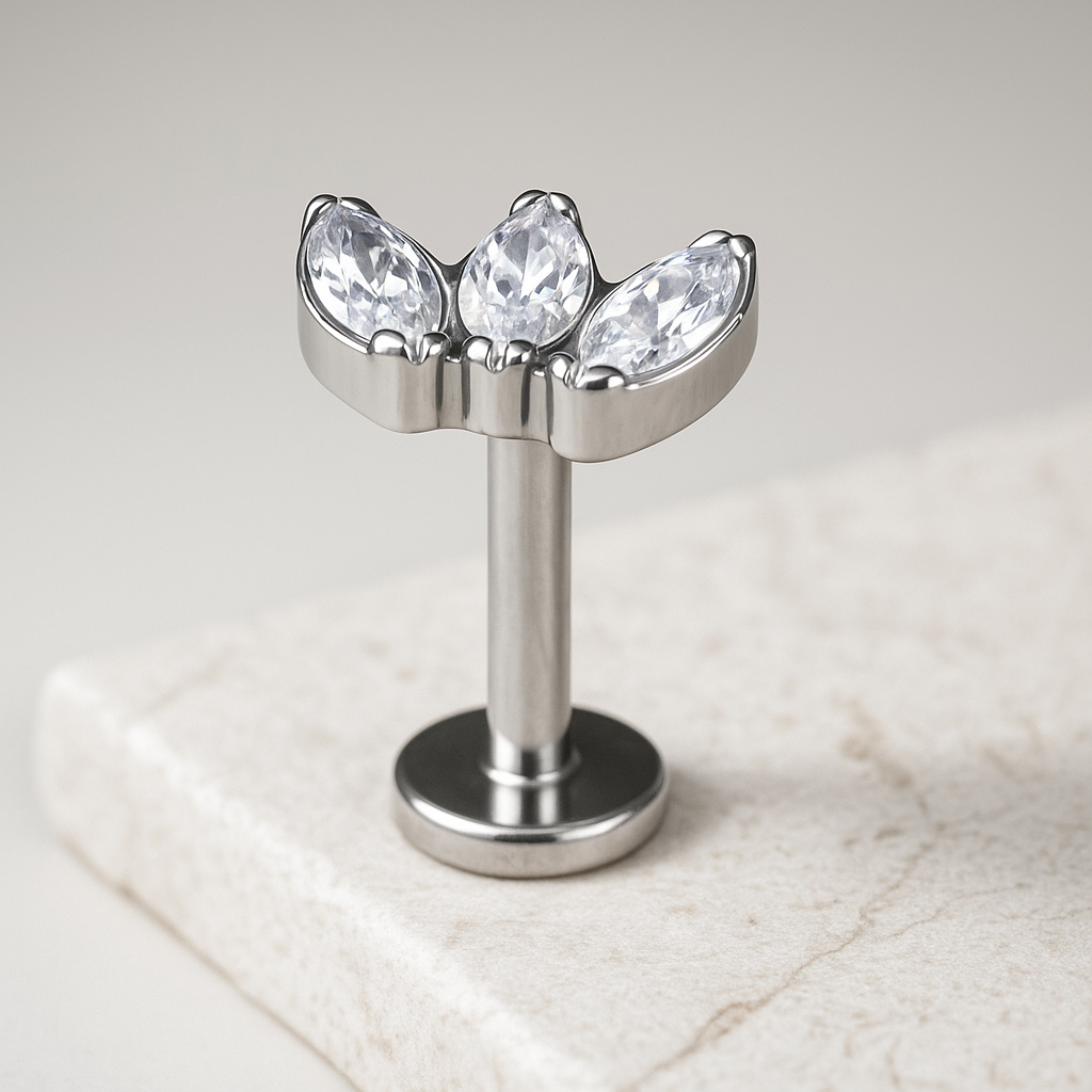Metallic jewelry piece with three clear gemstones on a marble surface