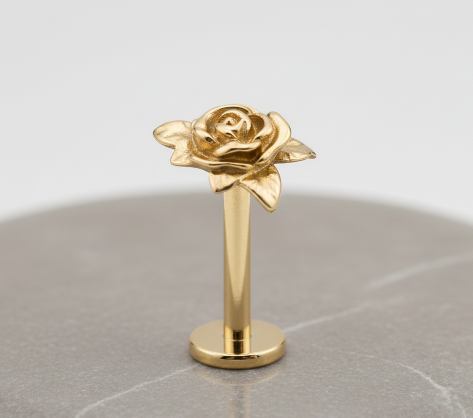 Gold rose-earringon a reflective surface with a light gray background