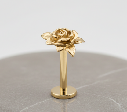 Gold rose-earringon a reflective surface with a light gray background