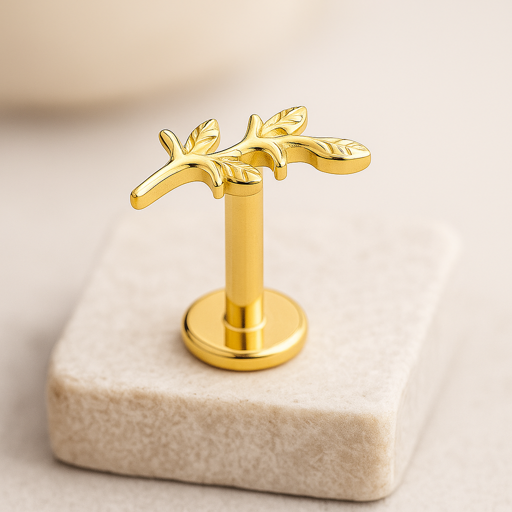 Gold jewelry labret stud with leaf design on a beige stone block