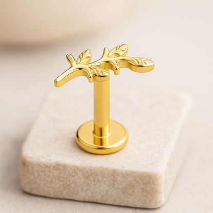 Gold jewelry labret stud with leaf design on a beige stone block